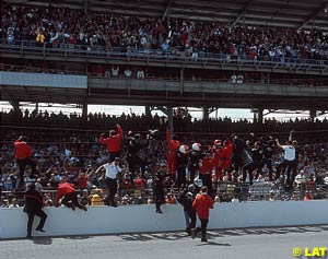 Helio Castroneves and his crew climb the fence at Indy