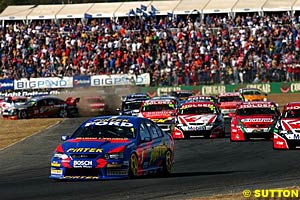 Marcos Ambrose leads into turn two on lap one as chaos erupts in the background