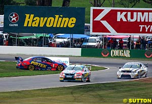 Marcos Ambrose sits stranded in the grass as teammate Russell Ingall and Craig Lowndes pass by